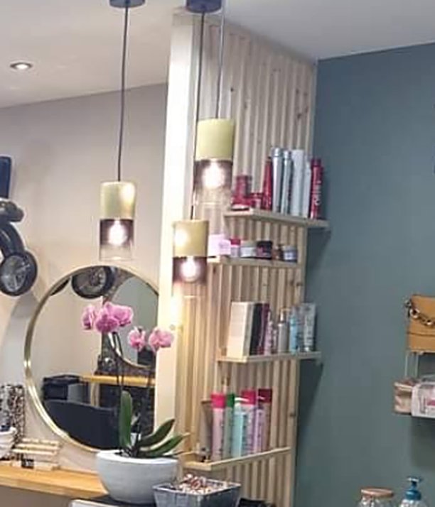 Détail du salon de coiffure Déesse Coiffure à Coudekerque-Branche : miroir, orchidée et étagère à produits